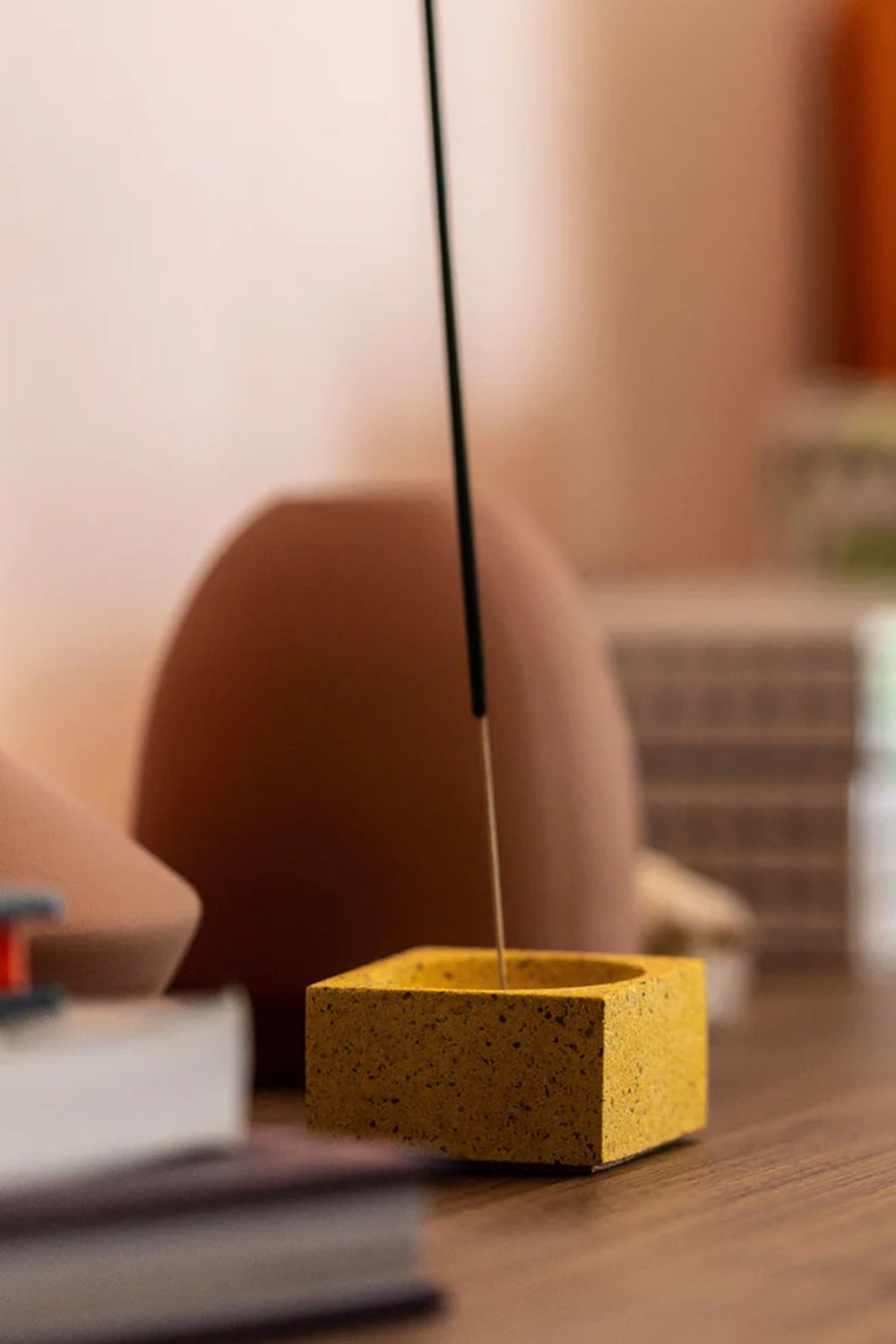 Close up of the marigold concrete terrazzo incense holder holding a stick of incense. 